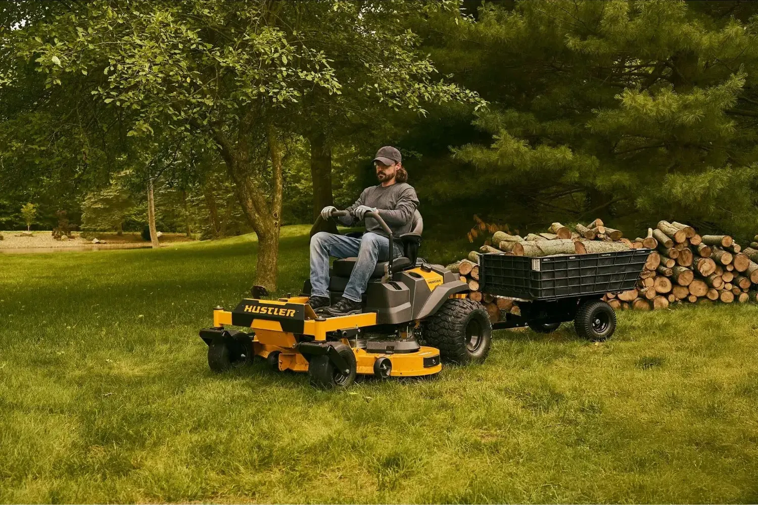 Hustler zero-turn pulling a light dump cart loaded with firewood